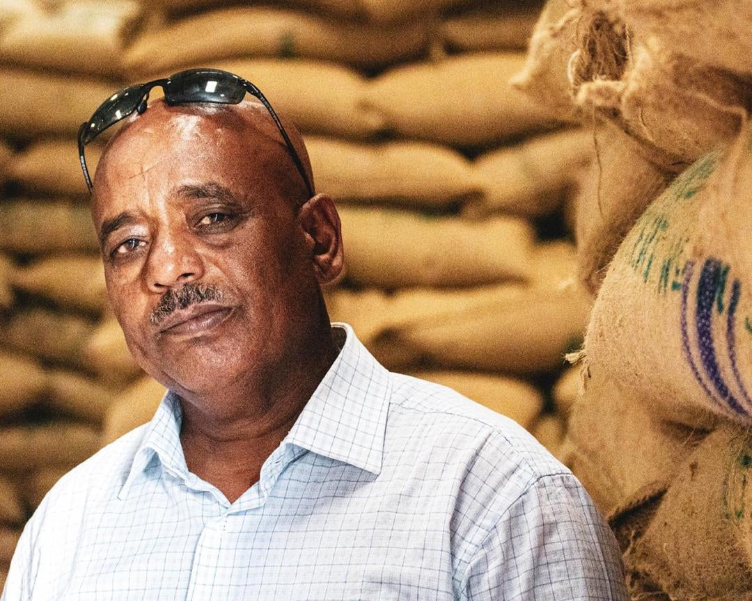 Mr. Hagos, longtime partner and washing station operator, standing in front of stacked burlap coffee sacks at Sere Saba, Ethiopia